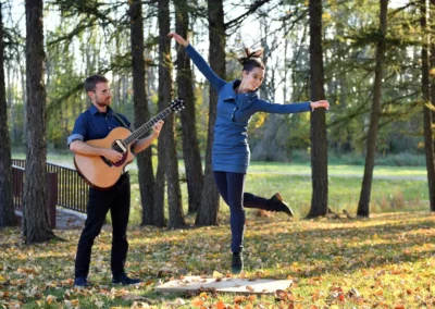 Mélissandre Tremblay-Bourassa saute en dansant aux côtés de François-Félix Roy jouant de la guitare en forêt.