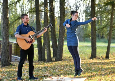 Mélissandre Tremblay-Bourassa saute en dansant aux côtés de François-Félix Roy jouant de la guitare en forêt.
