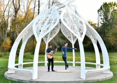 Danseuse et guitariste performant sous une grande structure architecturale blanche en forme de dôme ajouré.