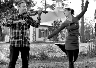 Photo noir et blanc d'un violoniste et d'une danseuse de gigue en pleine action dans un parc boisé.